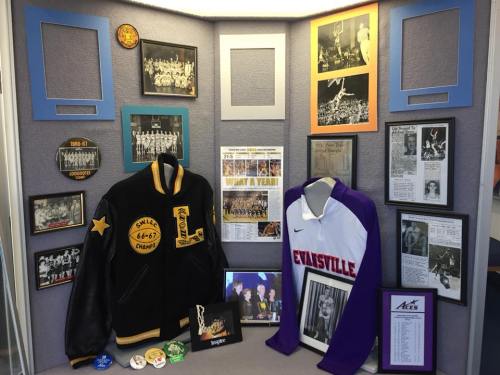 Display featuring sports memorabilia, including jackets, photos, and newspaper clippings celebrating a basketball team's history.