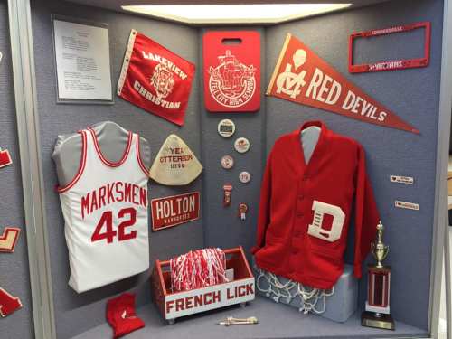 Display of red and white sports memorabilia, including jerseys, banners, and a trophy, showcasing local school pride.