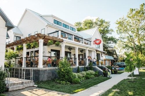 A charming restaurant with outdoor seating, surrounded by greenery and a clear blue sky.