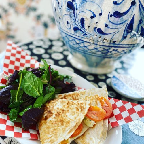 A plate with a quesadilla filled with tomatoes, served with a side salad, against a decorative background.