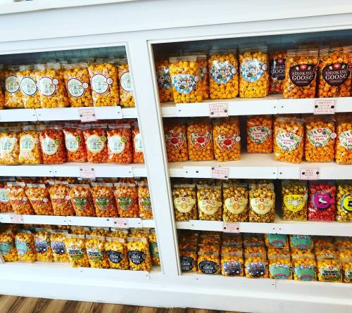 A display of colorful jars filled with various popcorn flavors on shelves in a store.