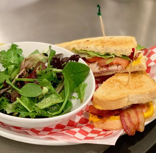 A sandwich with bacon, cheese, lettuce, and tomato, served with a side salad in a bowl.