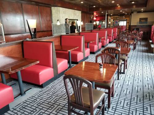 Interior of a restaurant featuring red booths, wooden tables, and a patterned carpet, with staff in the background.