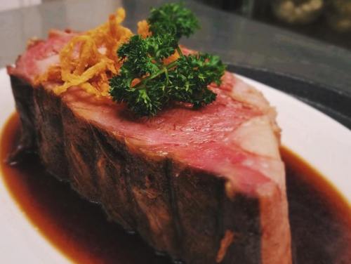 A slice of juicy meat topped with crispy onions and parsley, served on a plate with a rich sauce.