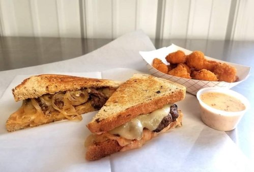 A toasted sandwich with melted cheese and onions, alongside a side of golden cheese curds and dipping sauce.