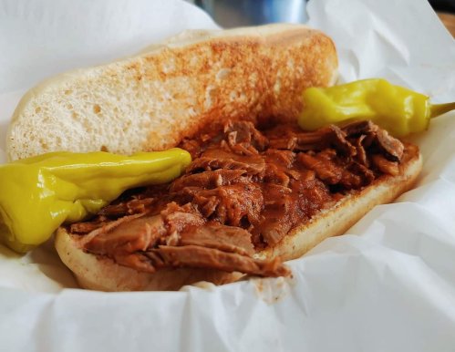A sandwich with tender beef, served in a toasted bun, accompanied by two yellow peppers on the side.