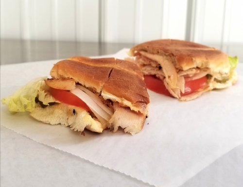 Two sandwiches with turkey, lettuce, and tomato on toasted bread, placed on white parchment paper.