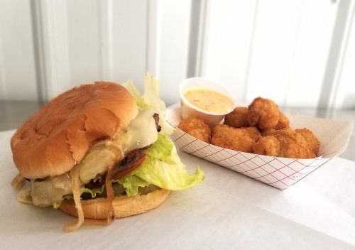 A juicy burger with melted cheese and lettuce, served with a side of crispy tater tots and dipping sauce.