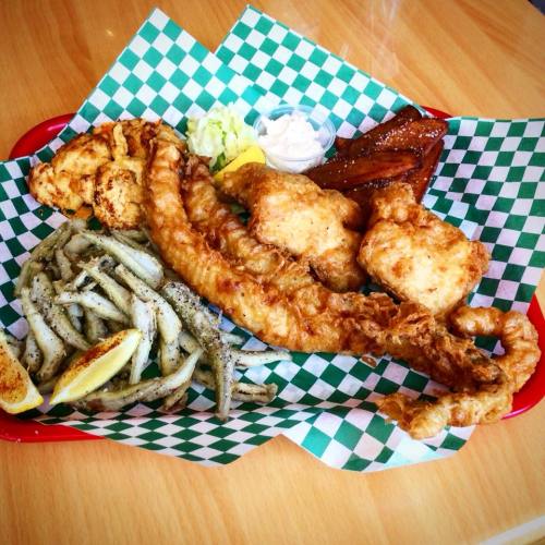 A platter of fried fish, hush puppies, fried okra, and dipping sauce on a green checkered paper.