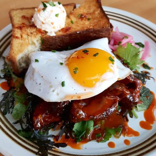A plate of fried egg on a bed of greens, topped with sauce, served with toasted bread and a dollop of cream.