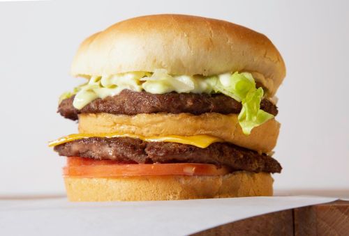 A stacked hamburger with two beef patties, lettuce, tomato, cheese, and mayonnaise on a soft bun.