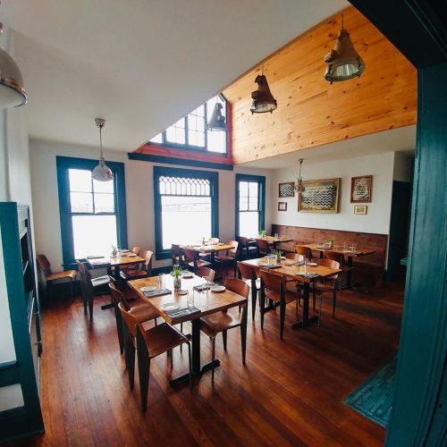 Cozy restaurant interior with wooden tables, chairs, and large windows, featuring a warm, inviting atmosphere.