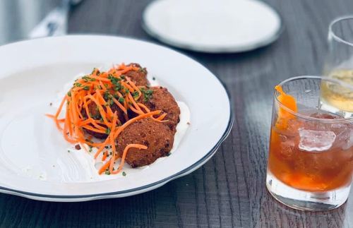 A plate with two golden-brown fritters topped with shredded carrots, served with a drink on the side.