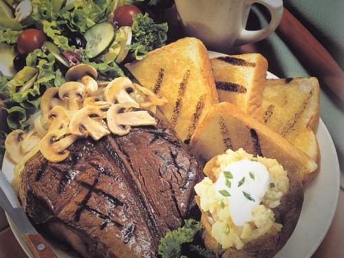 A plate featuring grilled steak topped with mushrooms, alongside grilled bread, a baked potato, and a fresh salad.
