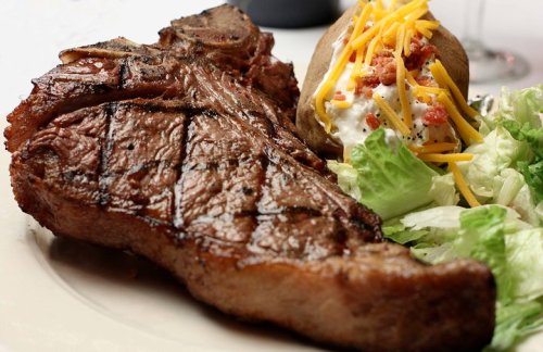 A grilled steak served with a baked potato topped with cheese and bacon, alongside a fresh green salad.