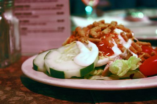 A colorful salad on a plate featuring lettuce, cucumbers, tomatoes, and crunchy toppings with dressing.