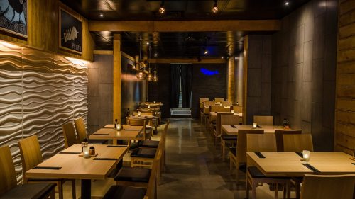 A modern restaurant interior with wooden tables, ambient lighting, and a textured wall design.