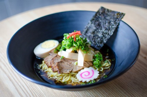 A bowl of ramen with sliced pork, green onions, bamboo shoots, a soft-boiled egg, and a piece of nori.