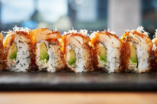 A close-up of sushi rolls with shrimp, avocado, and a drizzle of sauce, arranged neatly on a dark plate.