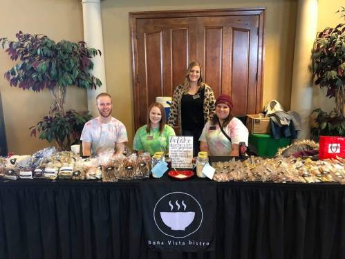 A group of four people stands behind a table filled with baked goods, promoting Bona Vista Bistro at an event.