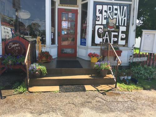Entrance of Serena Cafe with colorful flower pots, a welcome sign, and a closed notice on the door.