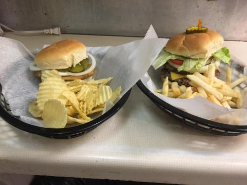 Two baskets of food: one with a burger topped with lettuce, tomato, and pickles, and the other with chips and fries.