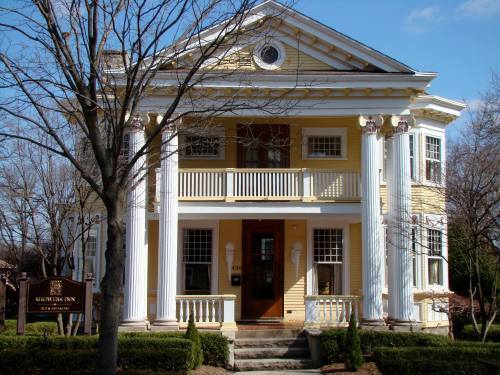A large yellow historic inn with white columns, a balcony, and a sign in front, surrounded by trees and blue sky.