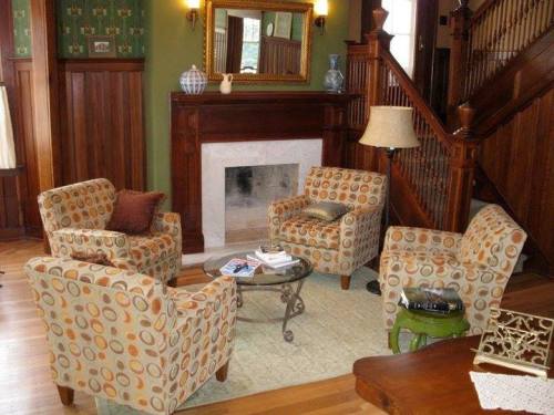 Cozy living room with patterned chairs, a round table, and a fireplace, featuring wooden accents and green walls.