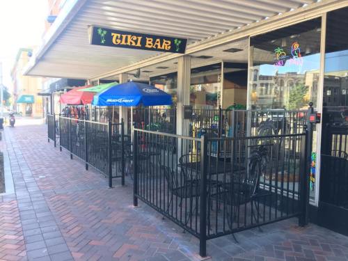 Outdoor seating area of a Tiki Bar with colorful umbrellas and a fenced patio on a brick sidewalk.