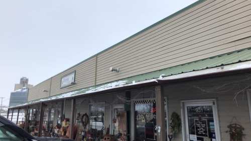 A storefront with a green awning, displaying various items, under a snowy sky with a building in the background.