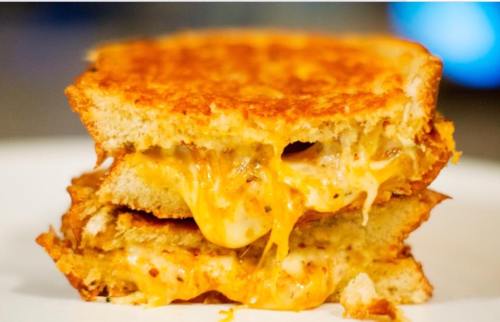 A stacked grilled cheese sandwich with melted cheese oozing between slices of golden-brown bread.