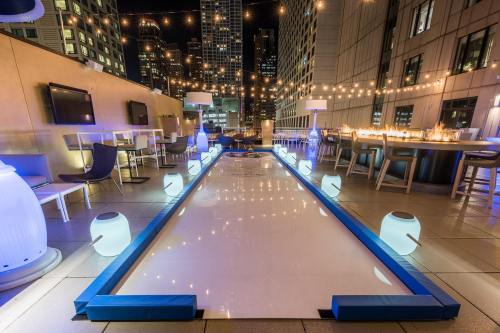 A rooftop lounge with a lighted ice rink, surrounded by modern seating and city skyline views at night.