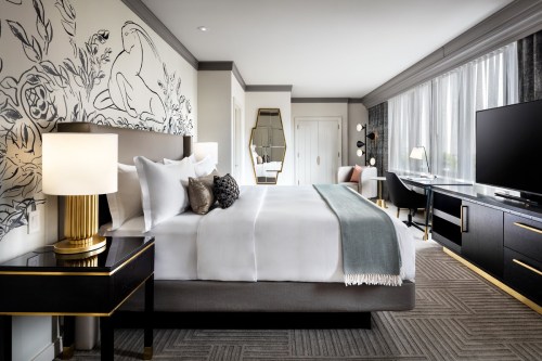 Modern hotel room featuring a king-sized bed, stylish decor, a large window, and a flat-screen TV.