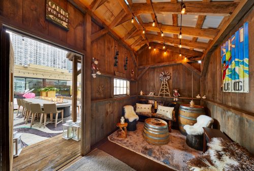 Cozy wooden cabin interior with barrels, soft seating, and warm lighting, leading to an outdoor dining area.