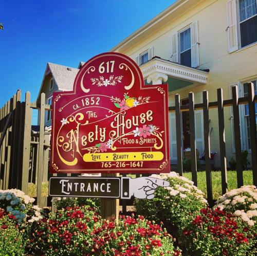 A colorful sign for The Neely House, established in 1852, with flowers and a welcoming entrance.