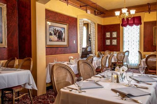 Elegant restaurant interior with white tablecloths, wicker chairs, and warm lighting, featuring artwork and floral centerpieces.