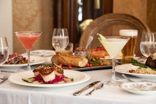 A beautifully set table with gourmet dishes, cocktails, and drinks, featuring scallops, bread, and various appetizers.