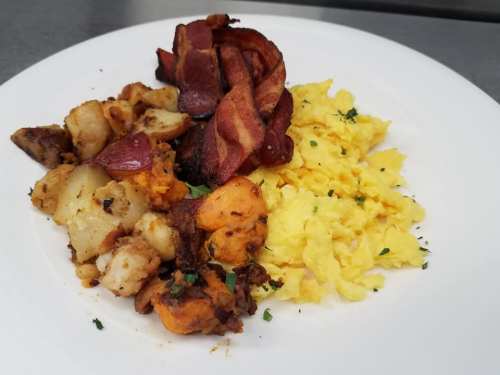 A plate of scrambled eggs, crispy bacon, and seasoned roasted potatoes garnished with herbs.