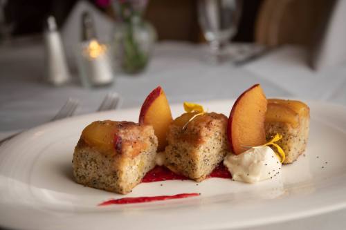 A plate with three pieces of cake topped with peach slices, served with cream and a drizzle of red sauce.