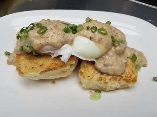 Two toasted biscuits topped with poached eggs and creamy sausage gravy, garnished with chopped green onions.