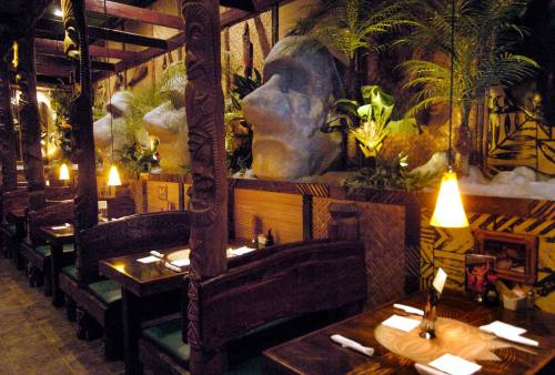 Interior of a themed restaurant featuring large stone heads, wooden booths, and tropical decor. Warm lighting enhances ambiance.