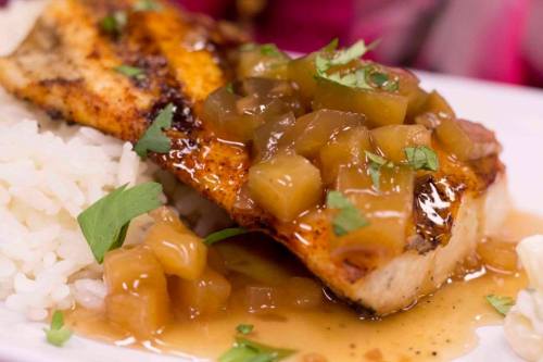 Grilled fish fillet topped with a savory sauce and diced fruit, served over a bed of white rice.