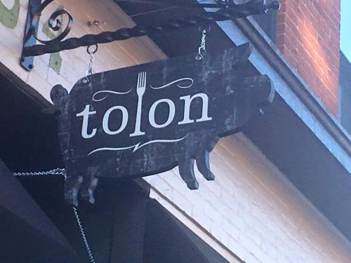 A rustic wooden sign shaped like a pig, featuring the word "tolon" and a fork design.
