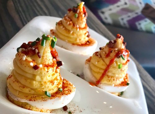 Three elegantly plated deviled eggs topped with spices, herbs, and a drizzle of sauce on a white dish.