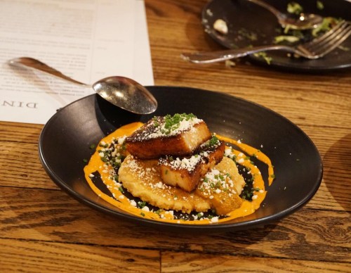 A black plate with two pieces of grilled polenta atop a creamy sauce, garnished with herbs and cheese.