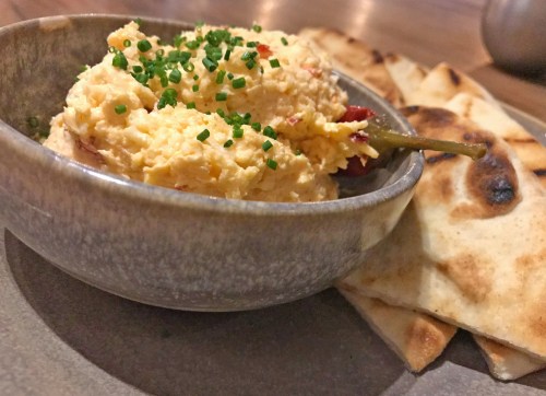 A bowl of creamy dip topped with chives, served with warm flatbread on a plate.