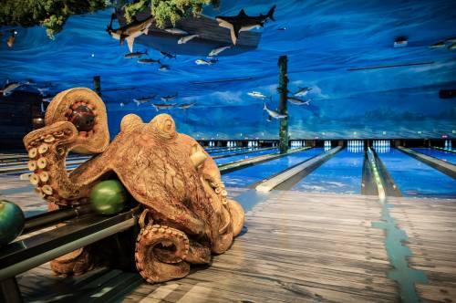 A whimsical bowling alley featuring an octopus sculpture and a vibrant underwater mural with sharks and fish.