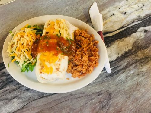 A plate with a burrito topped with cheese and salsa, served with rice and a side salad on a marble countertop.