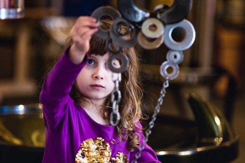 A young girl in a purple shirt examines metal rings and chains, showing curiosity and focus.
