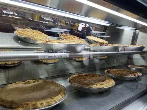 A display case filled with various freshly baked pies in metal pans.